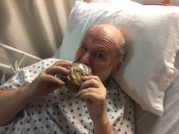 Ron eating large cookie in hospital bed